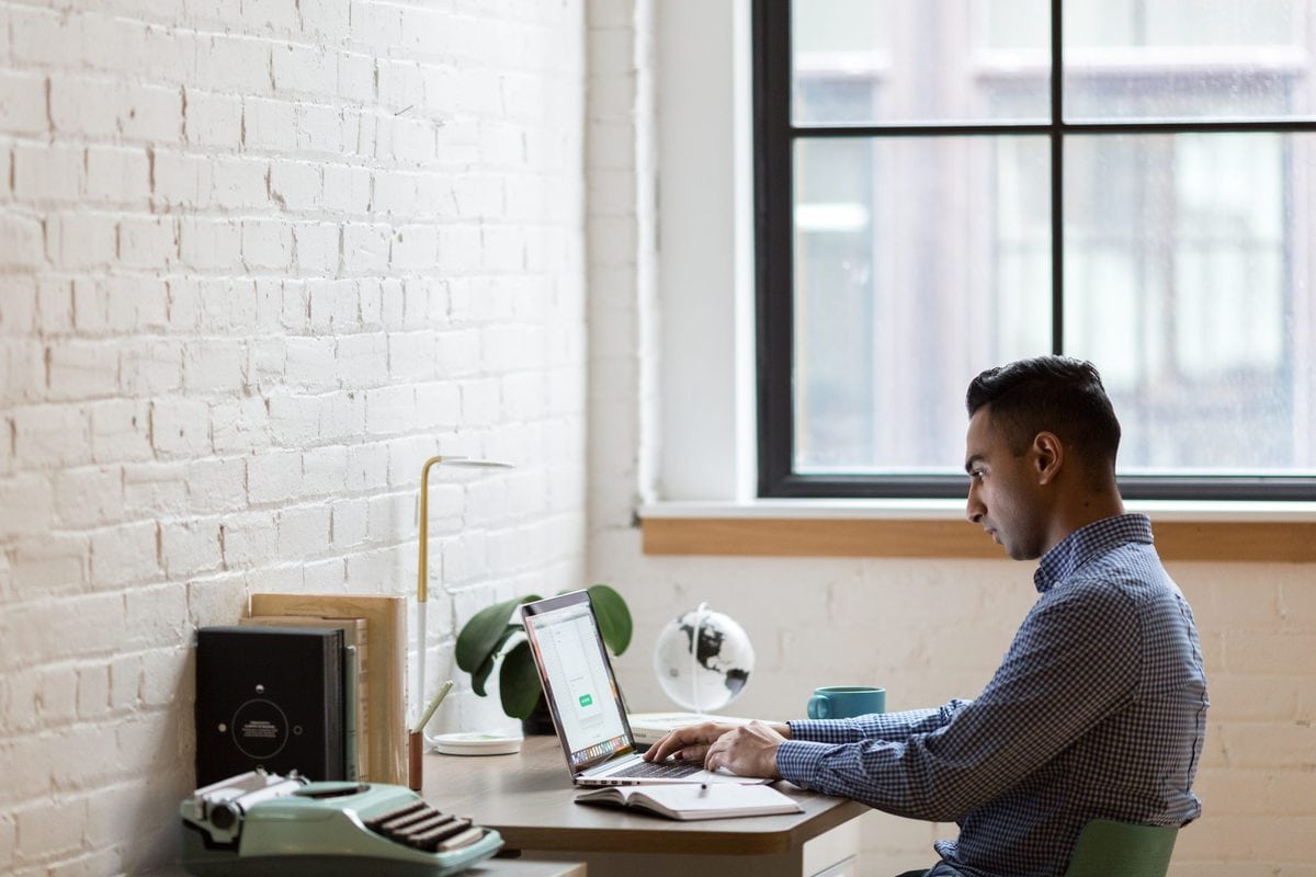 man sitting in green chair using laptop