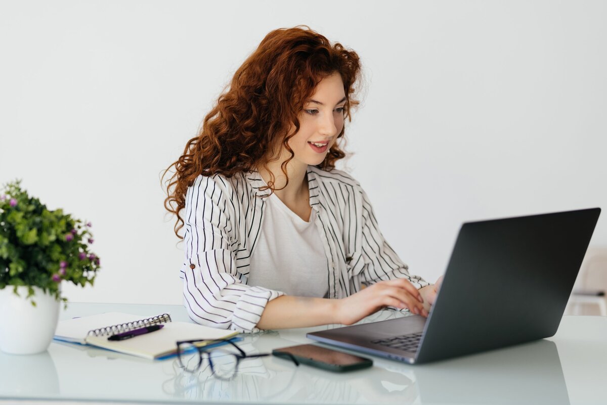 Ginger woman typing on laptop while sitting at desk in home